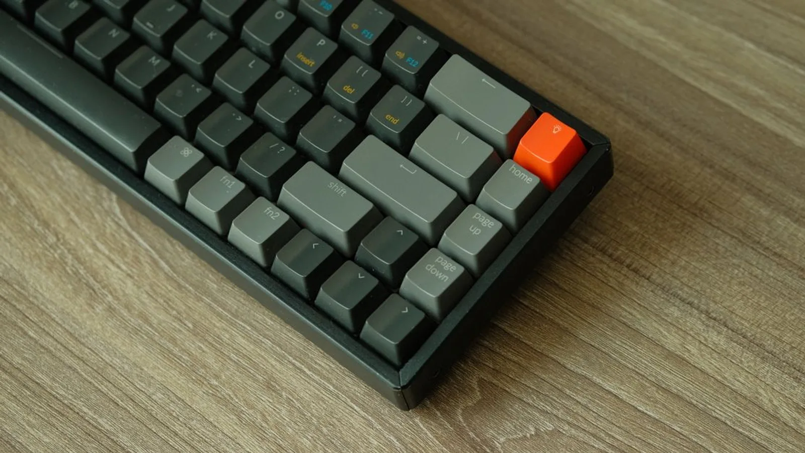 A detailed view of a mechanical keyboard with orange accent key on a wooden table.