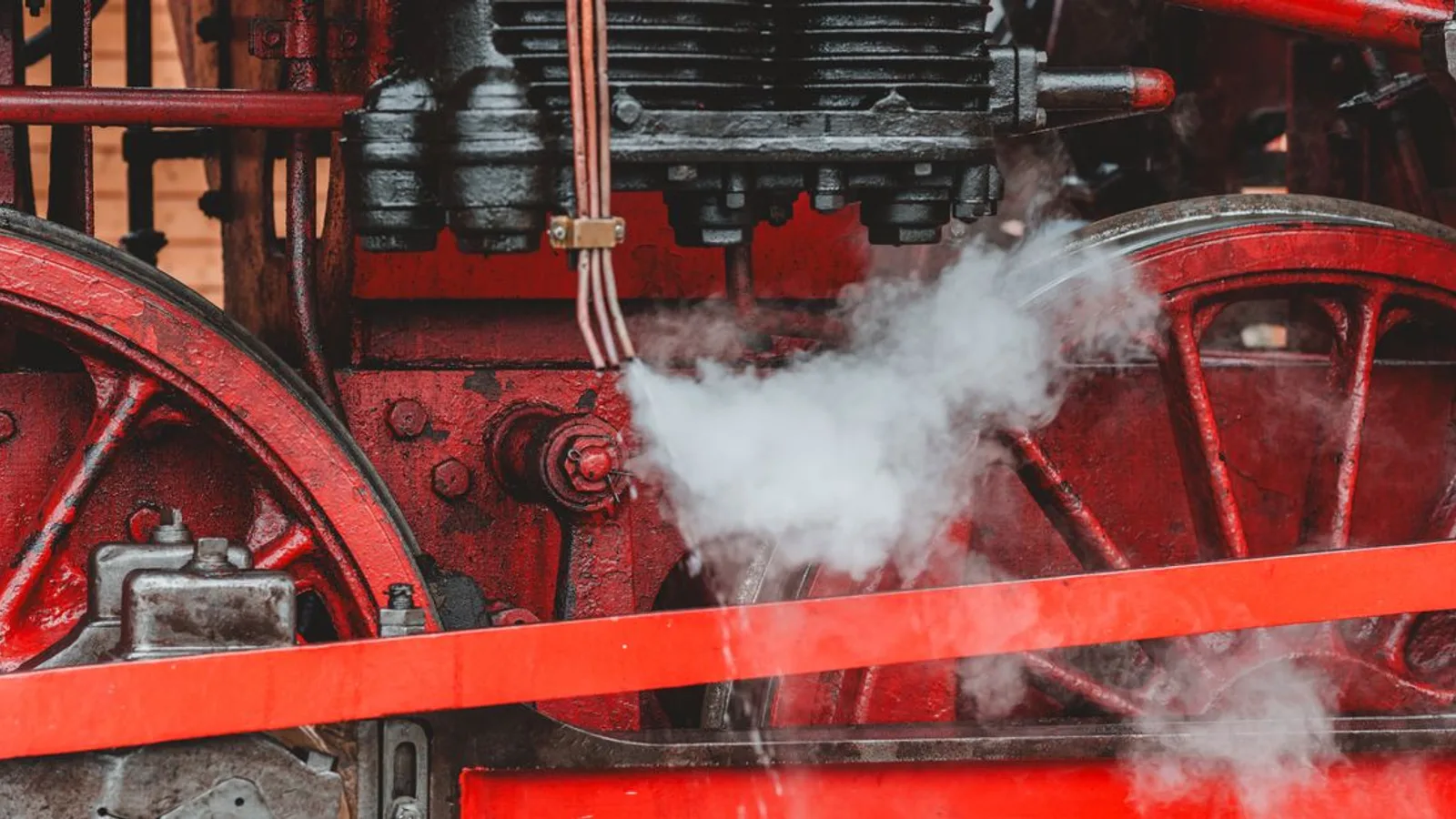 Detailed view of a red vintage steam locomotive engine showcasing gears and steam.