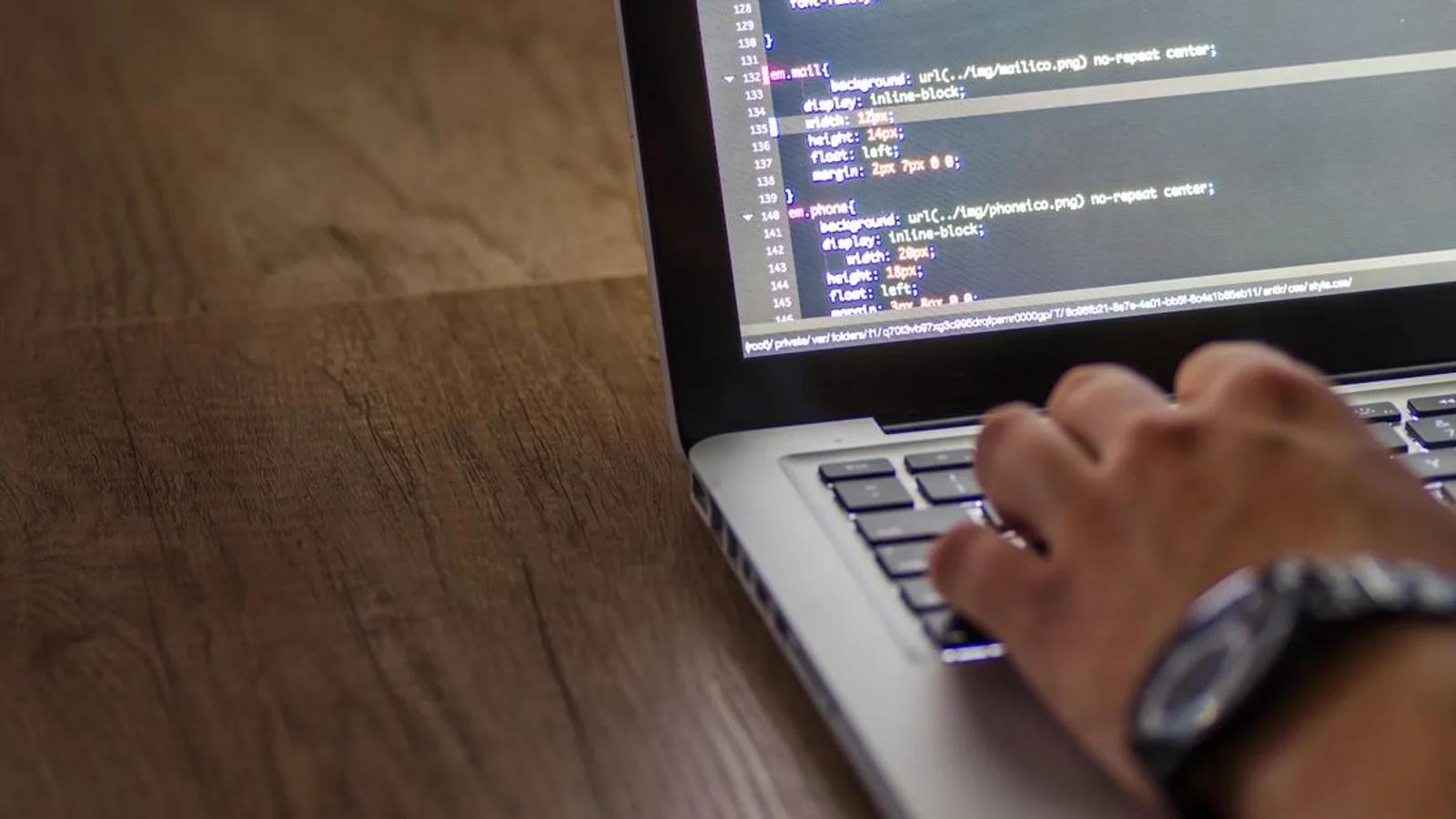 A person is typing code on a laptop, focusing on the screen with programming script.