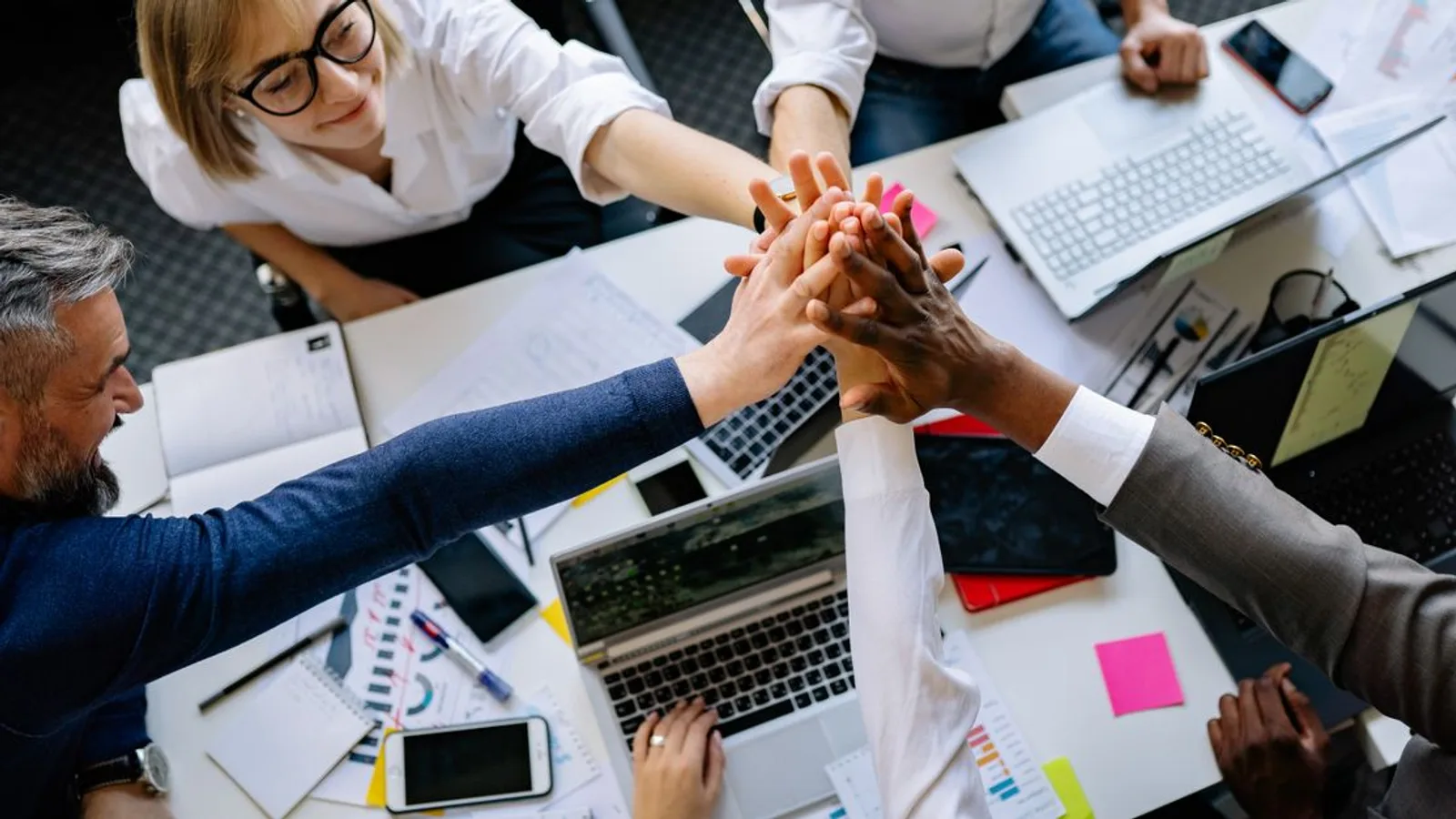 A group of diverse professionals high-fiving over a collaborative workspace.