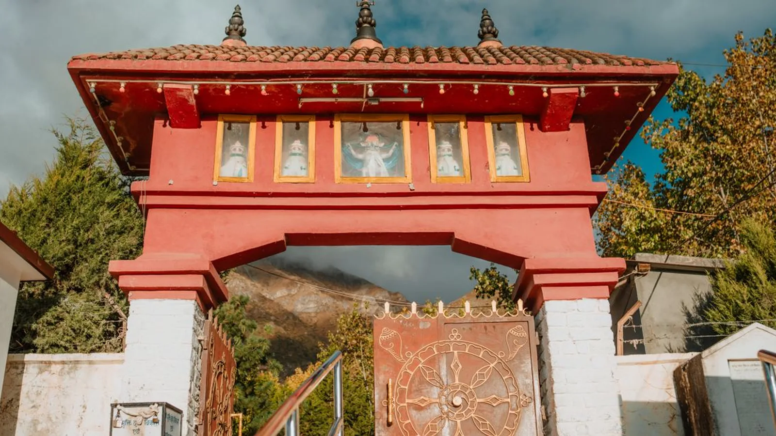 Outdoor view of a red traditional gateway with decorative gate and mountain backdrop.