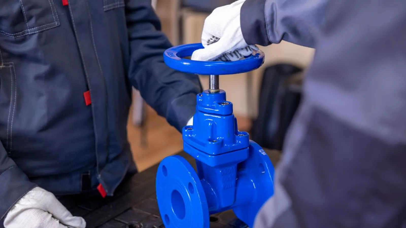Close-up of two technicians adjusting a blue industrial valve indoors.